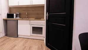 Une cuisine compacte avec des meubles blancs, un four à micro-ondes, une machine à café, un lave-vaisselle et une porte noire.