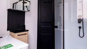 Une salle de bain avec une porte noire, des toilettes blanches, un miroir et une douche.
