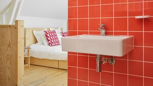 A bedroom with a wooden bed, white bedding, and a red-tiled wall with a white sink and mirror. - Chez Marie Jeanne -La Cite des Electriciens- 2pers (Bruay-la-Buissiere)