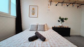 A neatly made bed with a patterned bedspread, two pillows, and rolled towels. A framed artwork hangs on the wall above the bed. - Atelier Wagram Au Coeur de Troucoing (Tourcoing)