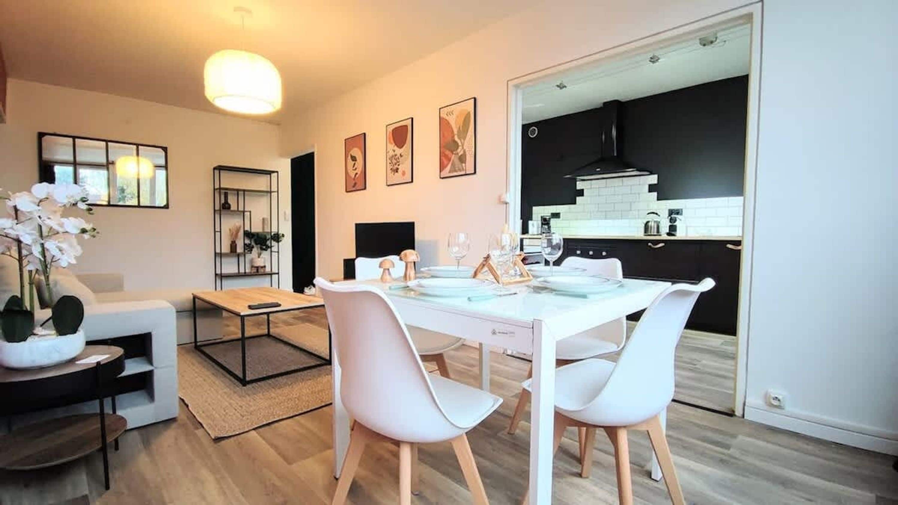 A modern living room with a dining area, a kitchen visible through an open door, and a large window.