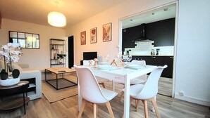 Ein modernes Wohnzimmer mit Essbereich, eine durchgehende Tür zur Küche und ein großes Fenster.