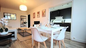 A modern living room with a dining area, a kitchen visible through an open door, and a large window. - Atelier Wagram Au Coeur de Troucoing (Tourcoing)