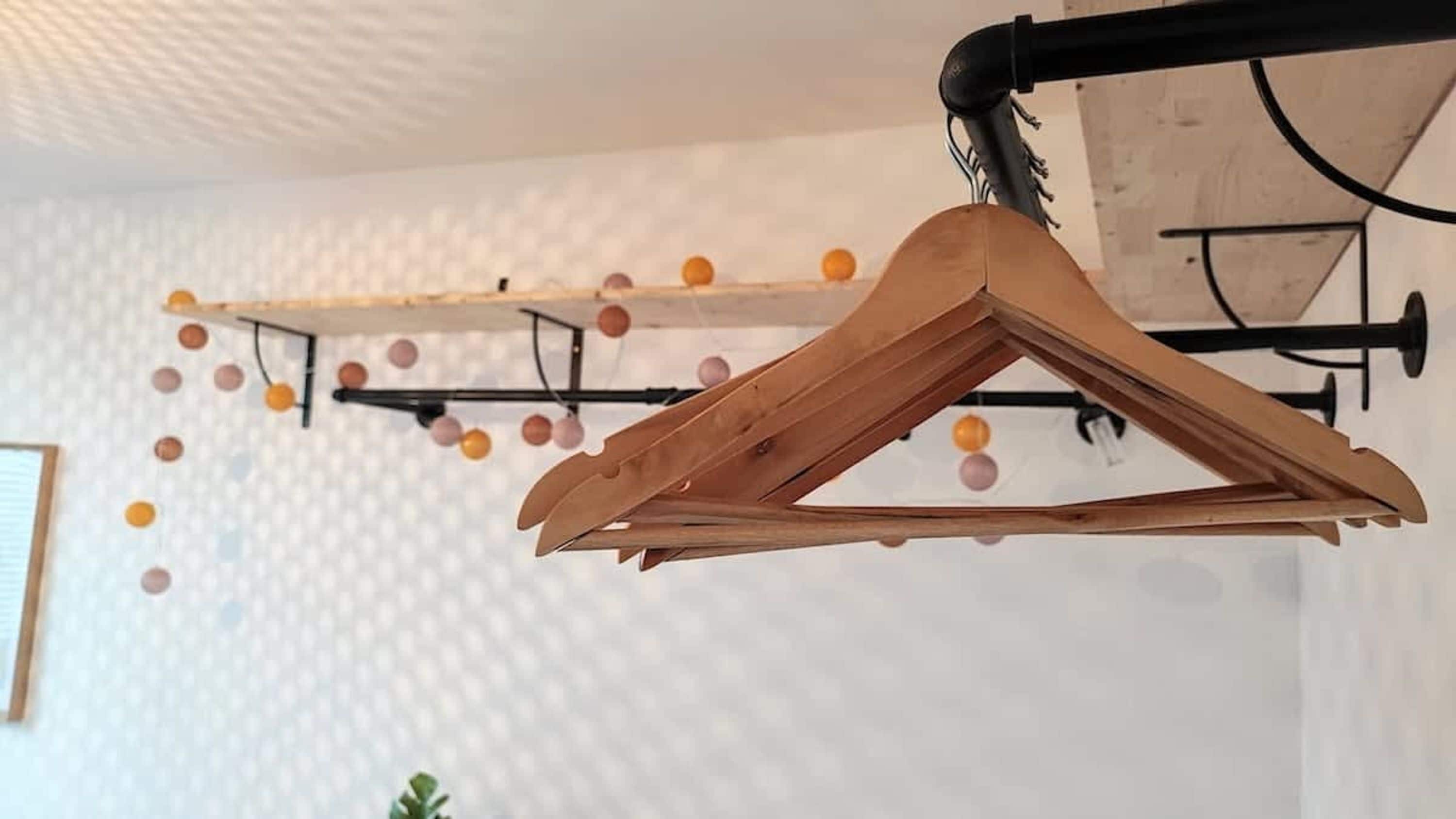 Un cintre en bois sur un portant en métal noir, avec un étendoir mural en arrière-plan.