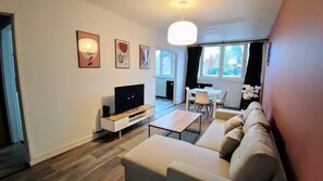 A modern living room with a flat-screen TV, a sofa, a dining table with chairs, and a large window with curtains. - Atelier Wagram Au Coeur de Troucoing (Tourcoing)