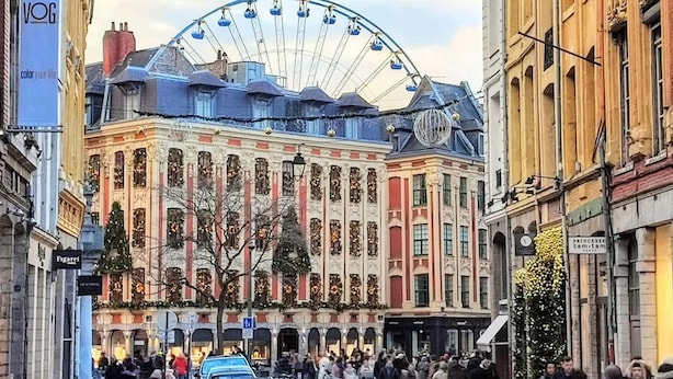 Ein historisches Gebäude mit einem großen Riesenrad im Hintergrund, einer Kopfsteinpflasterstraße und geparkten Autos.