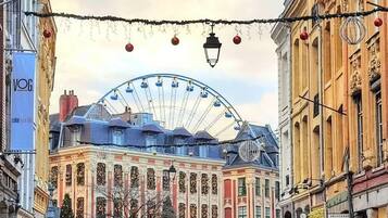 A historic building with a large Ferris wheel in the background, a cobblestone street, and parked cars.