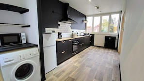 A compact kitchen with a washing machine, microwave, oven, and a black stove. - Atelier Wagram Au Coeur de Troucoing (Tourcoing)