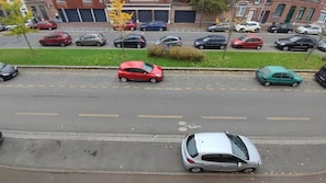 A street view with cars parked along the side, a grassy median, and buildings in the background. - Atelier Wagram Au Coeur de Troucoing (Tourcoing)