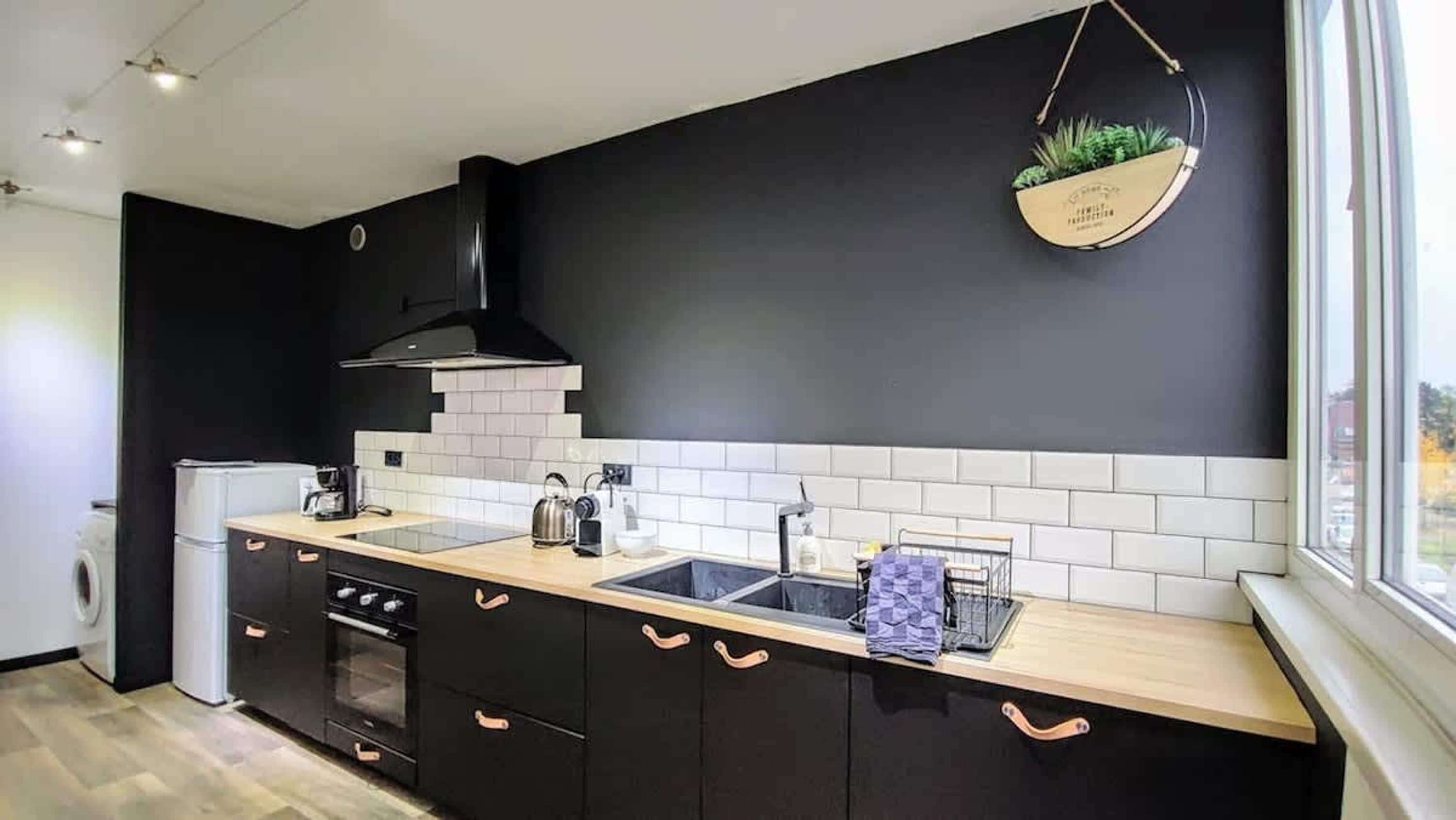 A modern kitchen with black cabinetry, a white tiled backsplash, a built-in oven, and a hanging plant.