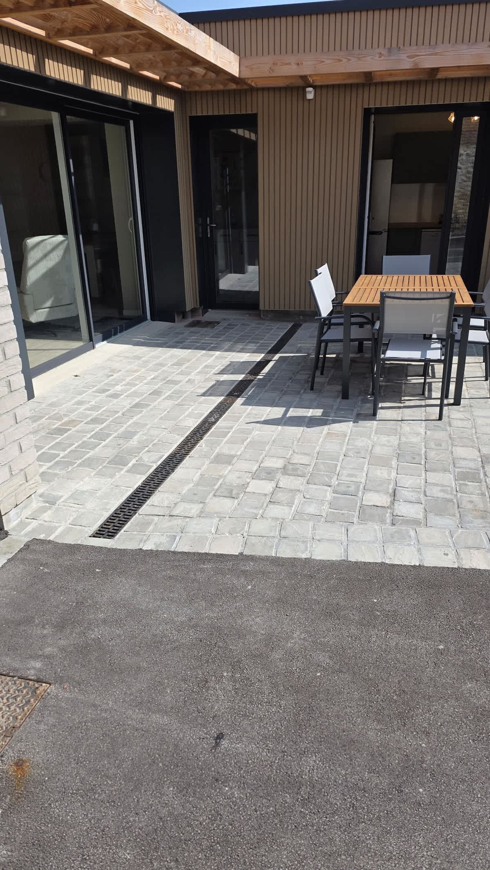 A patio area with a table and chairs, a drain, and a building with large glass doors.