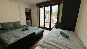 A bedroom with two beds, a sliding glass door to a patio, and a small desk area. - Maison 5 Chambres et Parking Gratuit (Arras)