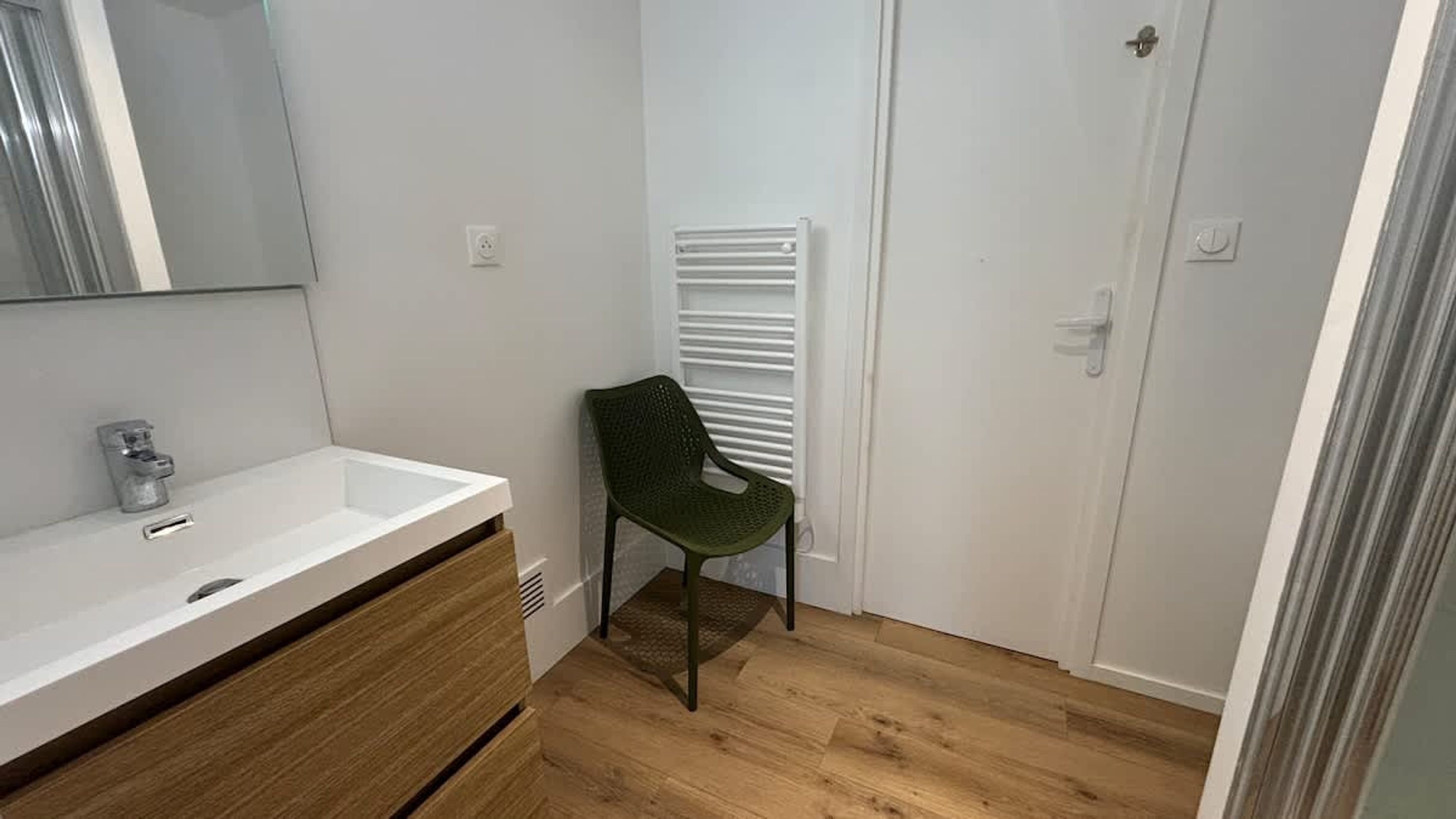 A bathroom with a white sink, wooden vanity, a green chair, a white radiator, and a door.