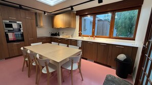 Une cuisine moderne avec des meubles en bois, une table à manger avec des chaises, un four encastré et une fenêtre donnant sur l’extérieur.