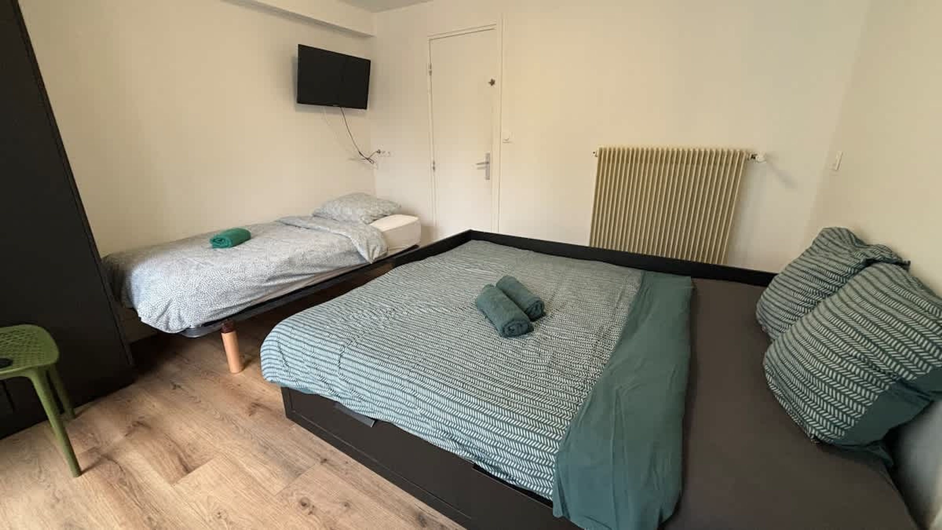 A room with a bed, a smaller bed, a TV, and a radiator.