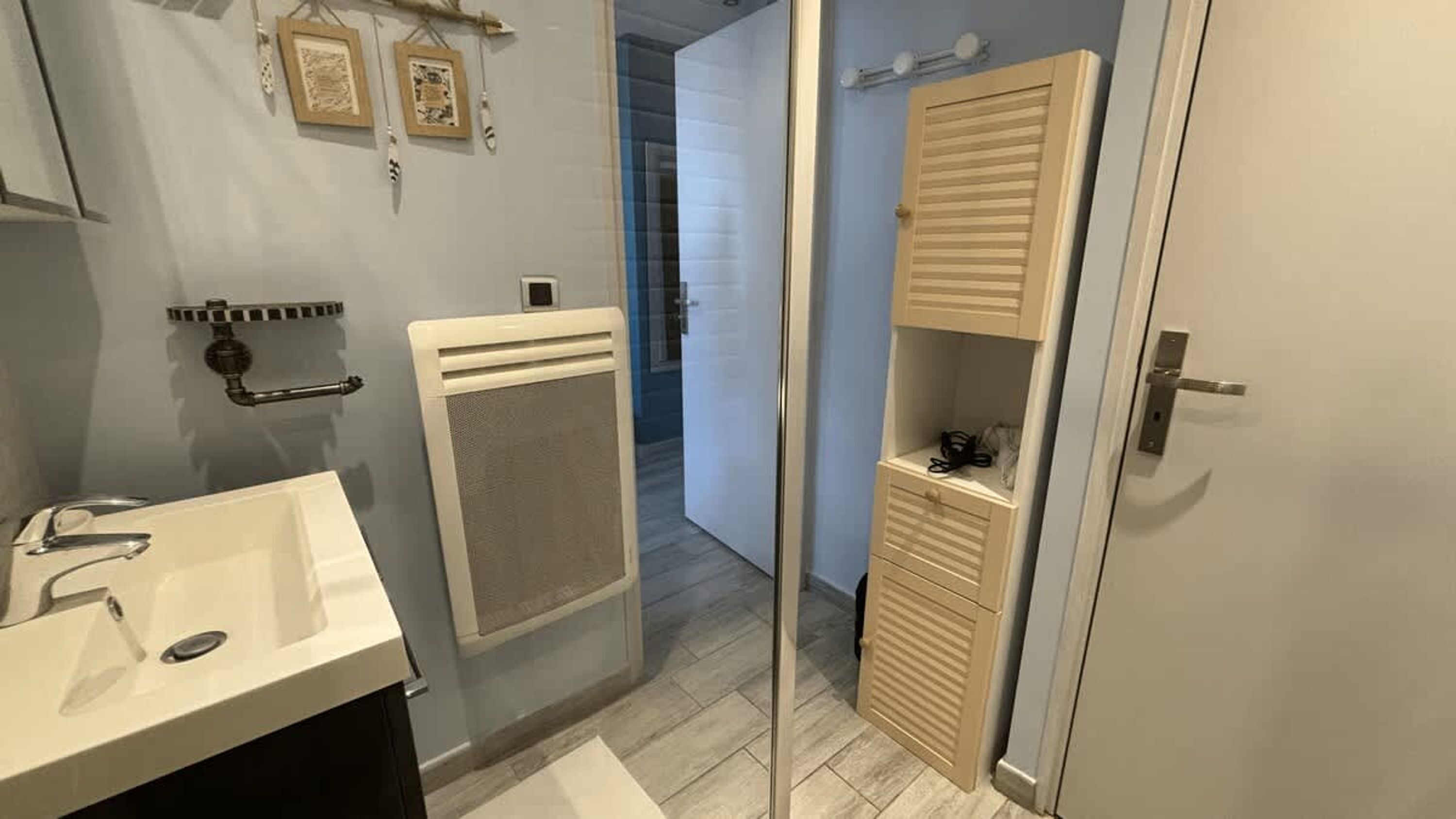 Une salle de bain avec un lavabo blanc, un porte-serviettes, un espace douche et un meuble à miroir.