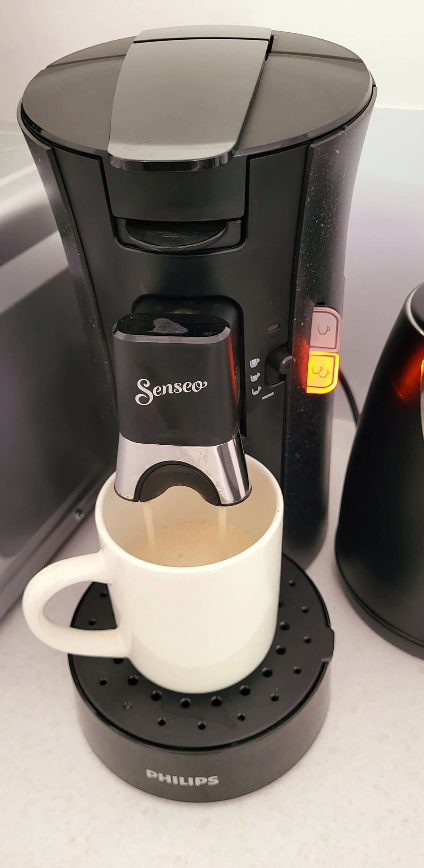 A Senseo coffee maker with a white mug on a Philips coffee pod holder.