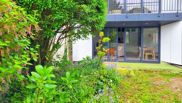 A modern two-story building with a glass balcony, a small garden area, and a visible outdoor seating arrangement. - Le Matisse - Centre - Jardin au Calme - Lumineux (Béthune)