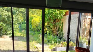 A room with a large sliding glass door leading to a garden, a table with chairs, and a hanging light fixture. - Le Matisse - Centre - Jardin au Calme - Lumineux (Béthune)