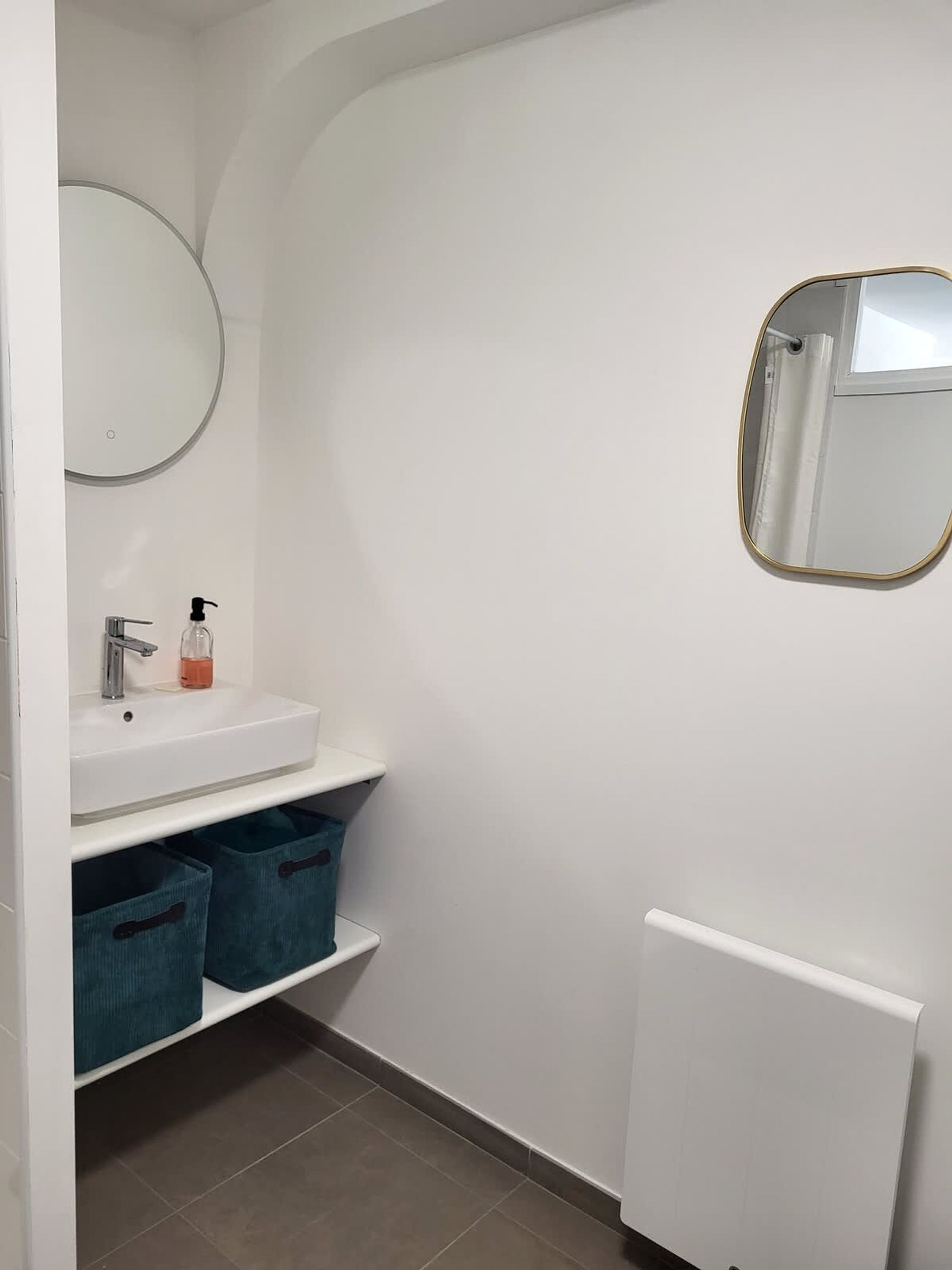 Une salle de bain avec un lavabo blanc, un miroir rond et un radiateur.