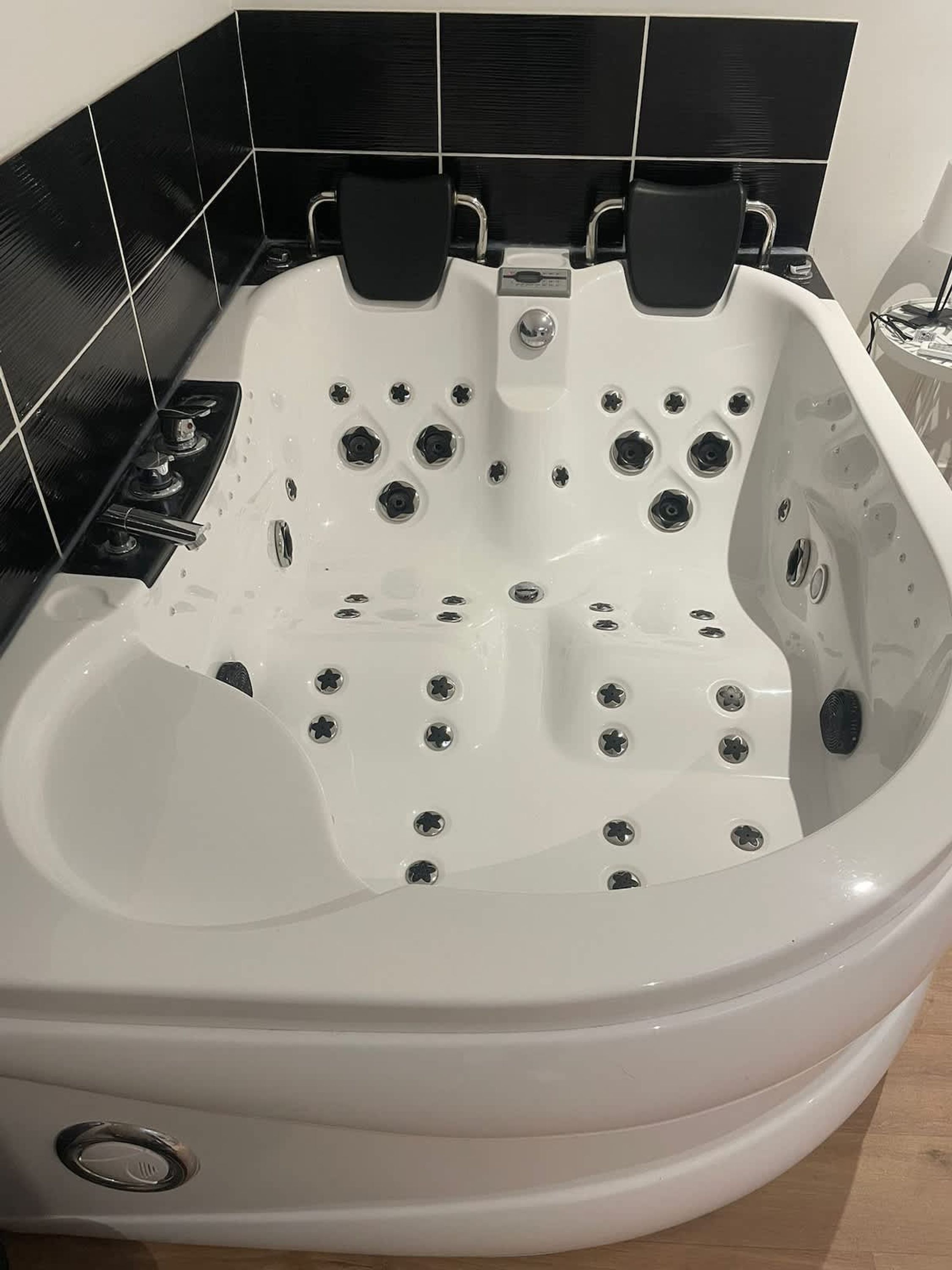A white bathtub with multiple jets and a control panel, set against a black tiled wall.