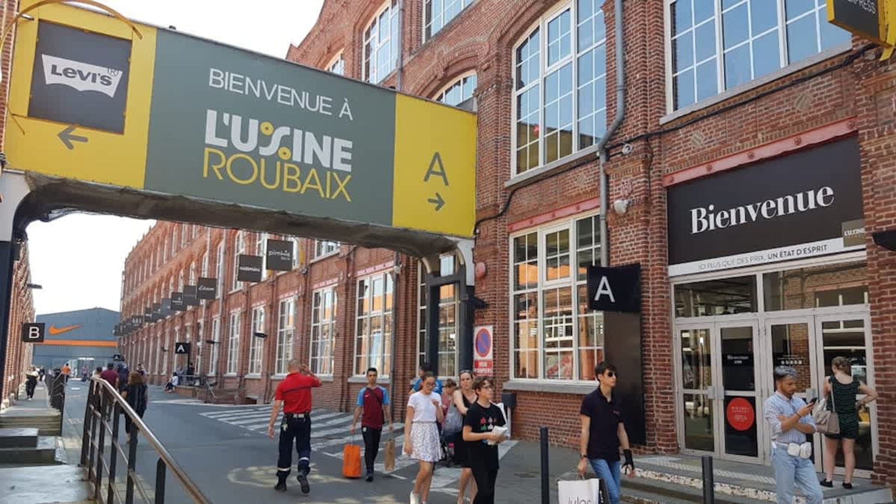 A street with a large sign for 'L'Usine Roulax' and a 'Bienvenue' sign above a building.