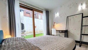 Quarto com cama, escrivaninha, cadeira, luminária e vista para o exterior.