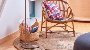 A wicker chair with a colorful cushion, a floor lamp, a woven rug, and a basket with books. - Chez Alice Sauna 4pers - La Cite des Electriciens (Bruay-la-Buissiere)