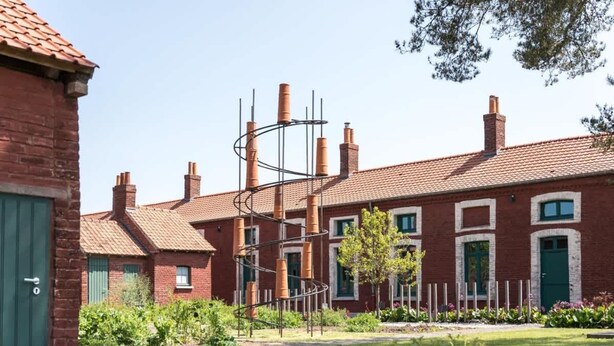 A brick building with multiple chimneys and a spiral metal structure in the yard. - Chez Alice Sauna 4pers - La Cite des Electriciens (Bruay-la-Buissiere)