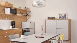 A compact kitchen with a microwave, coffee maker, and a refrigerator. There is a dining table with chairs and a pendant light above it. - Chez Alice Sauna 4pers - La Cite des Electriciens (Bruay-la-Buissiere)
