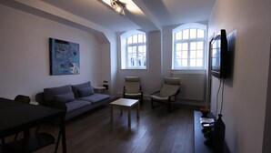 A living room with a sofa, two armchairs, a coffee table, and a TV mounted on the wall. - Villa Basecque Appartement 2 Chambres (Arras)