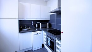 A compact kitchen with white cabinets, a microwave, a kettle, a dishwasher, and a stove. - Villa Basecque Appartement 2 Chambres (Arras)