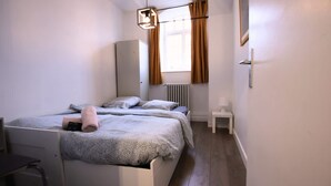 A bedroom with a bed, bedside table, lamp, radiator, window with curtains, and a hanging light fixture. - Villa Basecque Appartement 2 Chambres (Arras)