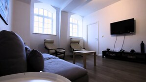 A living room with a sofa, two armchairs, a coffee table, a TV, and a fireplace. - Villa Basecque Appartement 2 Chambres (Arras)