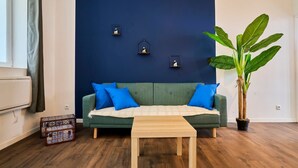 Habitación con sofá verde, cojines azules, una mesa de centro de madera, una planta en maceta y tres lámparas fijadas a la pared.