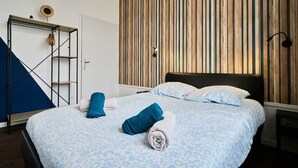 Una habitación de hotel con una cama, un panel de pared de listones de madera, una estantería metálica y una escalera azul.