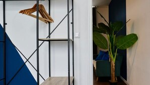 Una habitación con una estantería metálica, una planta en maceta y una pared azul.