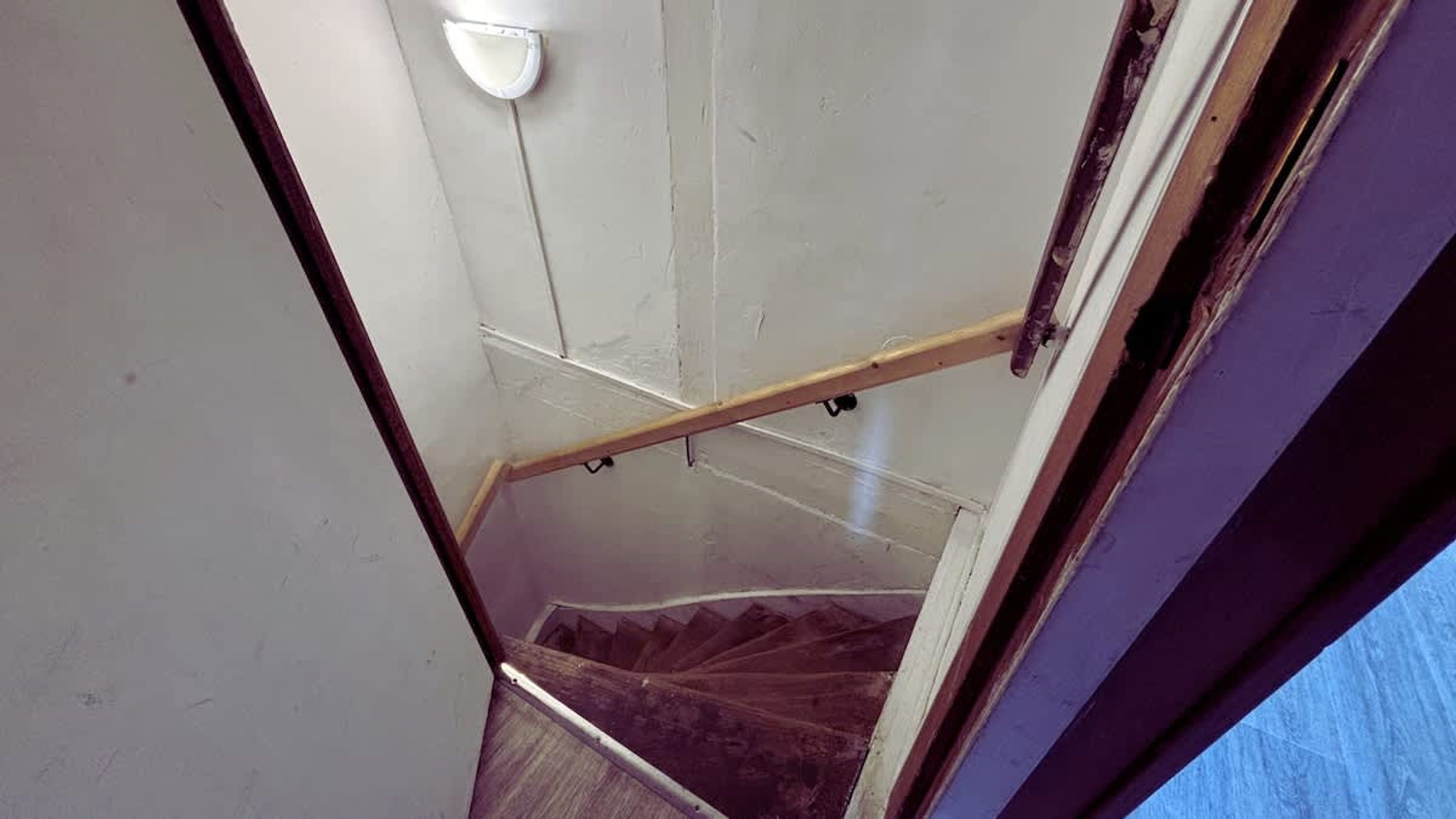 A staircase with a wooden handrail, a white wall, and a light fixture.
