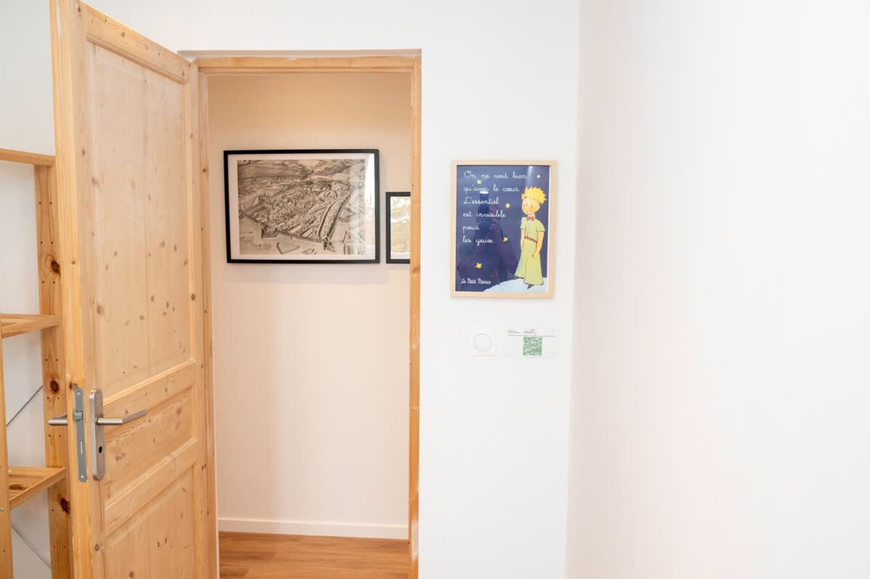 A hallway with a wooden door, a framed black and white drawing, and a poster with text and a cartoon character.