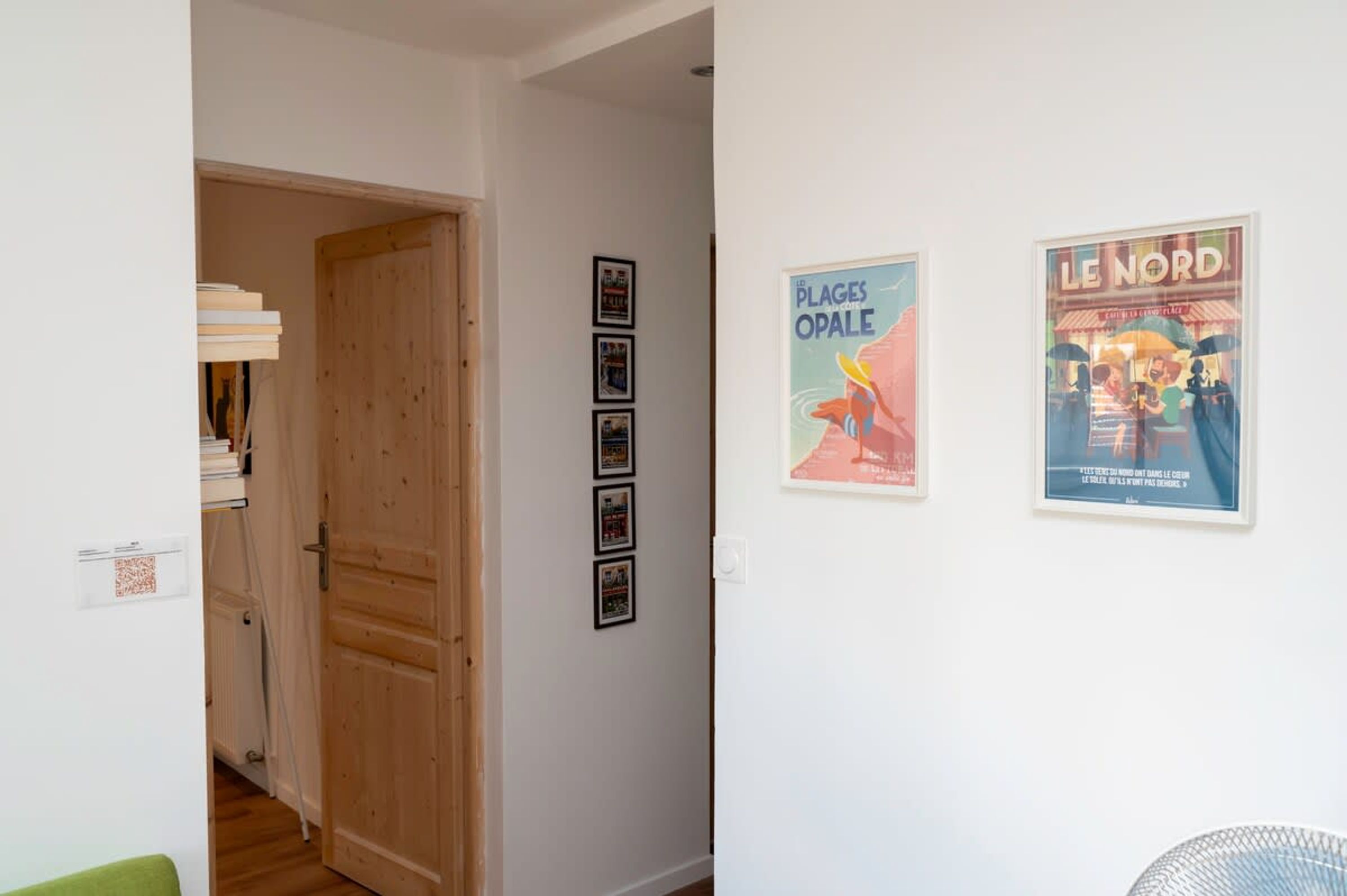 Un pasillo con puerta de madera, cuadros en la pared y dos carteles.