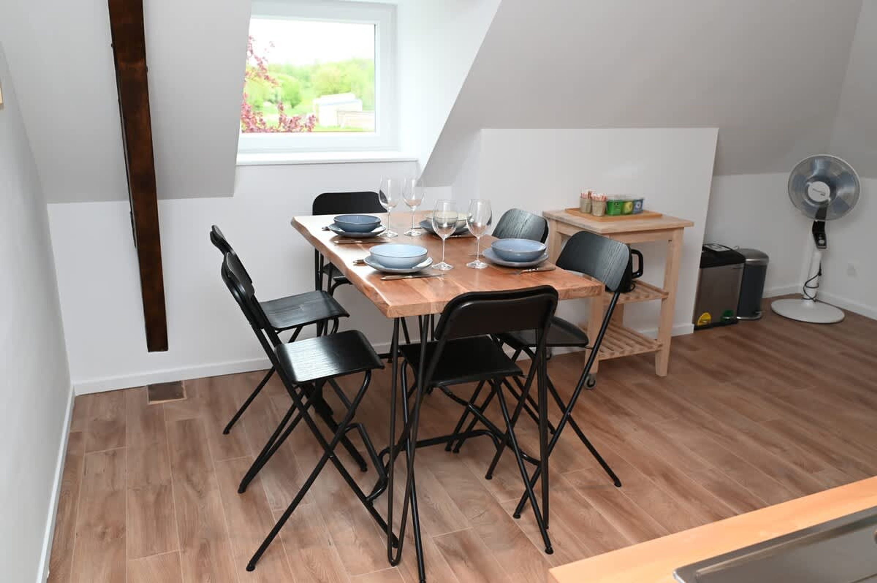 Un coin repas avec une table en bois, des chaises noires et une fenêtre donnant sur un paysage verdoyant.