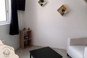 A room with a white sofa, a black table, a wooden shelf with decorative items, and two wall-mounted plant displays. - Chez Serge le N 105 Parking Gratuit 2 Pers (Noeux-les-Mines)