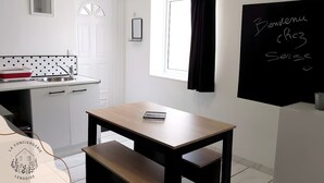 Ett litet, modernt kök med ett träbord, en svarta tavla där det står ”Välkommen till Serge”, och ett fönster med en svart gardin.