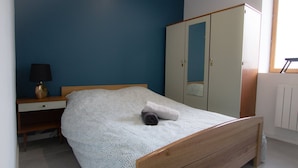A bedroom with a bed, a nightstand, a lamp, a wardrobe, and a window. - Player 1 Wifi Jeux Parking 4 Pers Lave Linge (Noeux-les-Mines)
