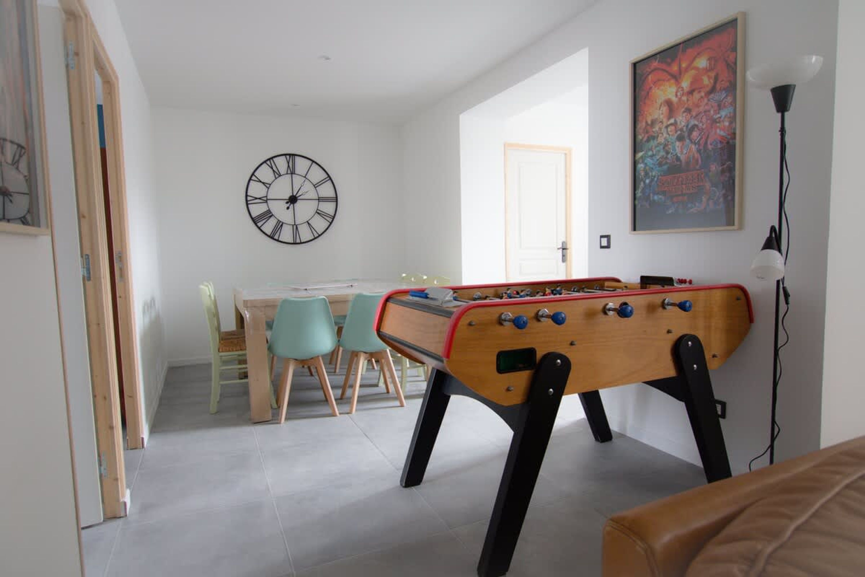A room with a foosball table, a clock, a door, and a poster on the wall.