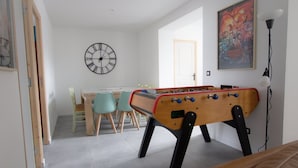 A room with a foosball table, a clock, a door, and a poster on the wall. - Player 1 Wifi Jeux Parking 4 Pers Lave Linge (Noeux-les-Mines)