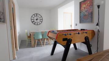 A room with a foosball table, a clock, a door, and a poster on the wall.