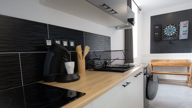 A modern kitchen with black and white tiles, a black induction cooktop, a wooden countertop, and a wall-mounted dartboard. - Player 1 Wifi Jeux Parking 4 Pers Lave Linge (Noeux-les-Mines)
