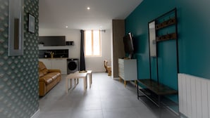 A modern living room with a sofa, coffee table, and a TV. There is a kitchen area with a washing machine and a dining table. - Player 1 Wifi Jeux Parking 4 Pers Lave Linge (Noeux-les-Mines)