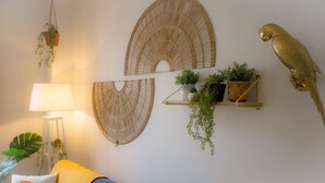 A room with a blue sofa, a hanging plant, a lamp, and wall-mounted decor including a bird sculpture and woven wall art. - Sublime 2 Bollaert 4 Pers Centre Ville (Lens)